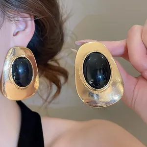 Macro detail of oversized vintage gold-tone earrings with black oval resin stone