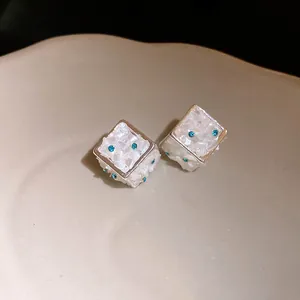 Primo piano dei piccoli orecchini a dado in argento con frammenti di conchiglia e cristalli