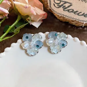 Detail shot of elegant floral stud earrings with blue zircons and pearls on white plate