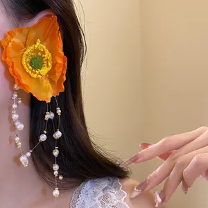 Detail view of a large orange flower earring with long beaded pearl tassels worn on ear.