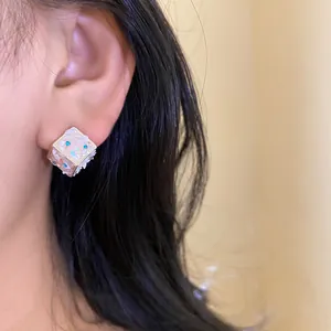 Dettaglio dell'orecchino a cubo con strass blu e trama a conchiglia sull'orecchio.