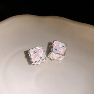 Vista macro di conchiglie rosa testurizzate e strass blu scintillanti su orecchini a perno