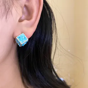 Primo piano di un orecchino a bottone a cubetto azzurro effetto ghiaccio tritato sull'orecchio
