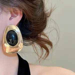 Close-up view of a vintage gold oval stud earring with black resin center worn on ear