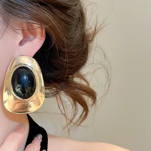 Detailed close-up showing vintage gold oval earrings with black resin stone on a model