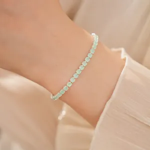 Gros plan d'un bracelet en argent avec des zircons ronds vert menthe sur un poignet.