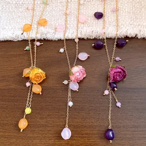 Three color options of resin preserved rose necklaces with tassels on a wooden surface.