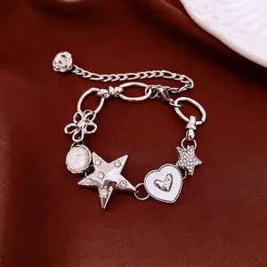 Bracelet à breloques argenté avec étoiles en strass et cœur sur fond en tissu marron.