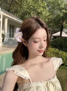 Gros plan de barrettes à fleurs de cerisier en tissu rose portées sur le côté.
