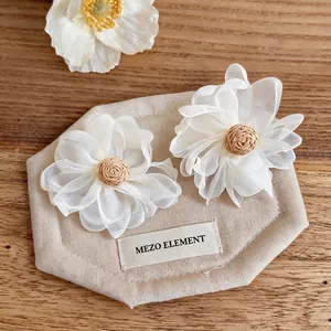 Handmade raffia woven flower stud earrings with white fabric petals for summer vacation style.