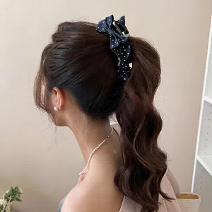 Detailansicht einer dunkelblauen Polka-Dot-Schleifen-Haarklammer in gewelltem Haar.