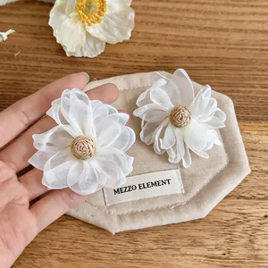 Close-up of white mesh flower earrings with woven raffia centers for summer style