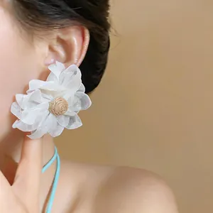 Close-up of oversized white raffia flower earring with woven center on model