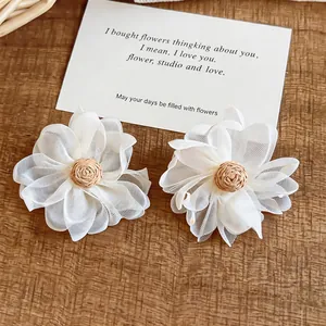 Detailed macro view of white fabric flower earrings with woven raffia centers.
