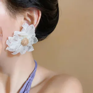 Close-up of elegant oversized white mesh flower earring with woven raffia center