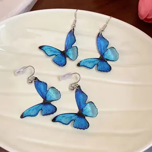 Translucent blue resin butterfly earrings with glitter wings on a ceramic plate