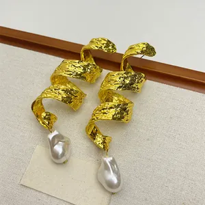 Detailed macro view of golden spiral twisted metal earrings featuring large baroque pearls
