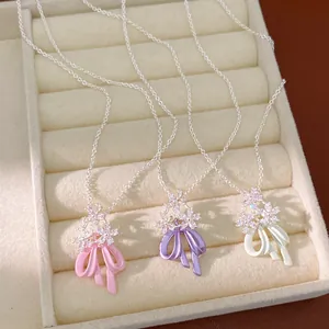 Primo piano di eleganti ciondoli a fiore di zircone e fiocco in smalto rosa, viola e bianco.