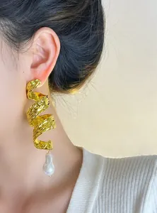 Close-up detail of gold spiral earrings with baroque pearl drop in vintage heavy metal style