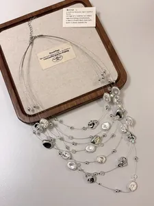 Vista dettagliata di una collana a più strati argento con perle irregolari su legno.