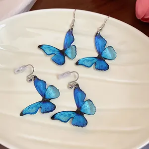 Detailed view of blue resin butterfly earrings with glitter on a white ceramic plate