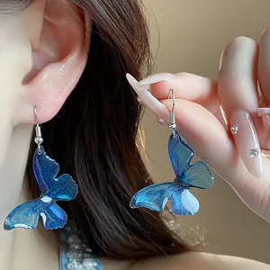 Detailed view of blue resin butterfly drop earrings on ear and hand