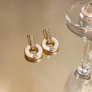 Primer plano de elegantes pendientes de aro dorados con nácar blanco y circonitas