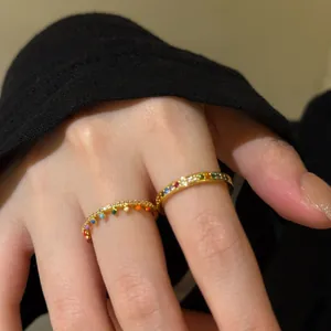 Close-up of elegant stackable gold rings with vibrant rainbow zircons on fingers