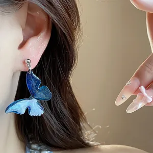 Close-up detail of blue resin butterfly earrings on ear with glitter and silver hardware