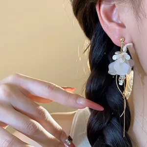 Close-up detail of elegant white flower tassel earring with golden finish worn by model