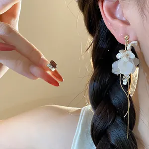 Close-up detail of elegant white floral drop earrings with long tassels worn by model