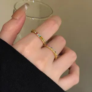 Close-up of two delicate rainbow gold rings with colored zircon stones on a finger