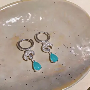 Elegant zircon moon and blue waterdrop silver hoop earrings displayed on a beige plate