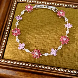 Close-up of a vintage-style bracelet with pink zircon flowers on green velvet background.