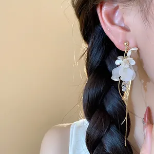 Elegant French-style white flower earrings with long gold tassels shown on a model.