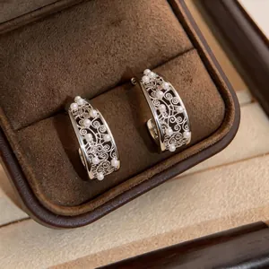 Elegant C-shaped silver stud earrings with intricate hollow floral patterns and pearls.