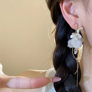Close-up of elegant French style white floral earrings with long gold tassel detail.