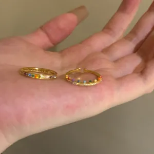 Close-up detail showing two minimalist gold-tone rings with colorful rainbow zircon stones