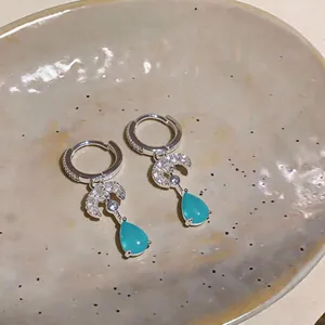 Close-up of silver hoop earrings with zircon crescent moon and a blue teardrop stone drop
