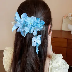 Detailed view of a light blue fabric flower hair clip with tassel worn on dark hair.