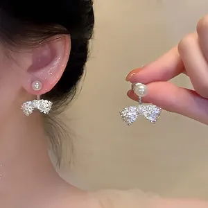 Close-up of sparkling silver bow earrings with pearl stud shown on ear and held by hand