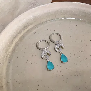Detailed macro shot of elegant silver moon and blue teardrop earrings on a beige ceramic dish