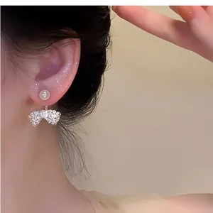 Close-up detail of a model wearing elegant French-style pearl and sparkling bow stud earrings.