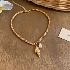 Close-up of gold twisted rope choker with seashell and pearl pendants on wood