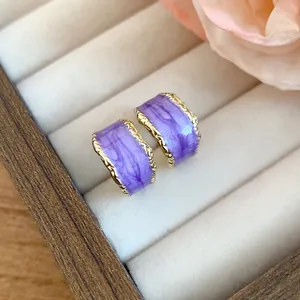 Primo piano di orecchini a C vintage in smalto viola marmorizzato con bordi dorati.