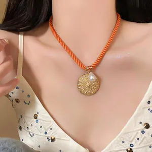 Detail shot of an orange rope necklace with gold disc and pearl pendant on model.