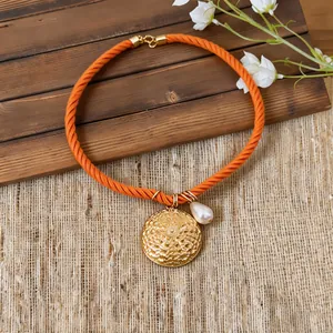 Close-up of orange rope necklace with gold textured round pendant and pearl detail