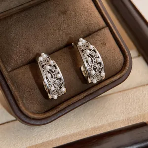 Detailed macro view of silver filigree C-shaped earrings with pearls in a brown jewelry box