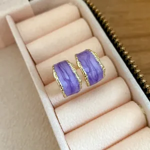Dettaglio orecchini a C in smalto viola con bordo dorato in un portagioie elegante
