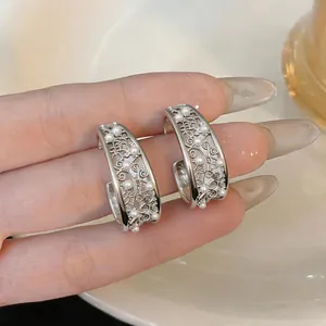 Detailed macro view of ornate hollow silver C-shaped earrings with dainty white pearls